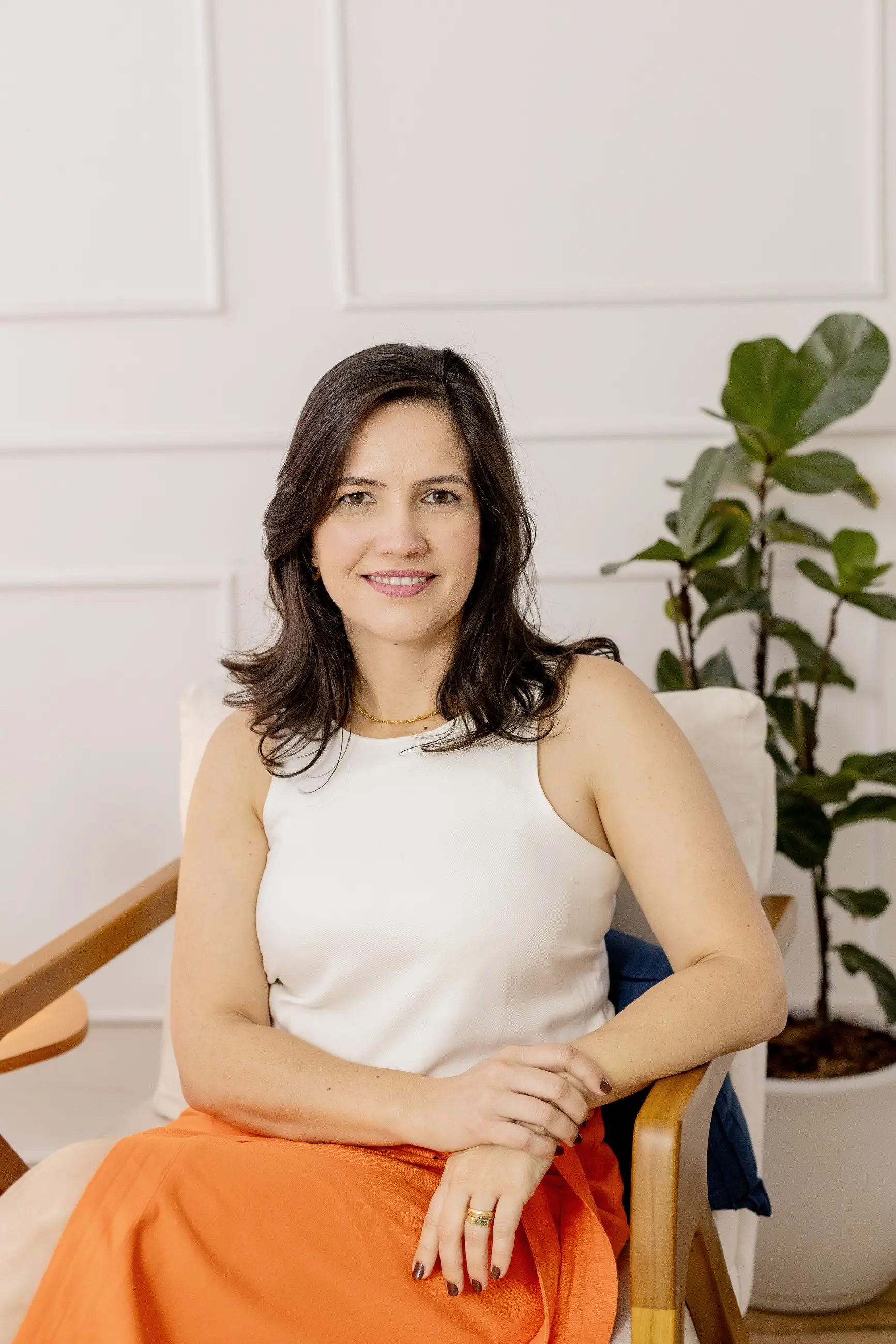 Dani Oliveira sentada em uma poltrona, sorrindo para a câmera